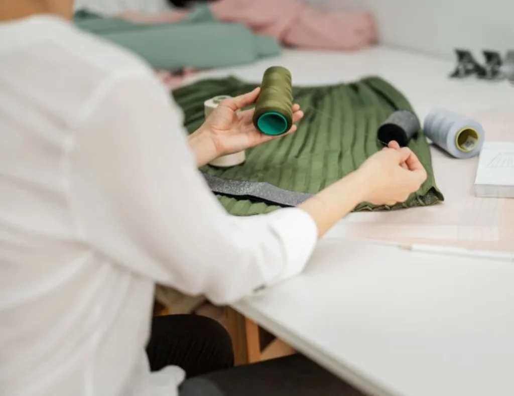 Fabricante de ropa sostenible inspeccionando hilos y tejidos durante la producción de prendas